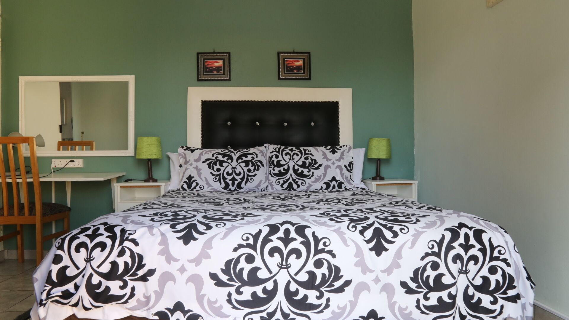 Une chambre à coucher comprenant un lit, un bureau, deux lampes, une chaise et deux tableaux encadrés accrochés au mur.