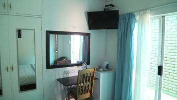 A room with a desk, chair, mirror, television, and a window with curtains.