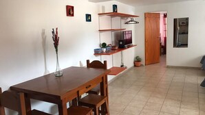 Un comedor con una mesa y sillas de madera, un florero con flores y estantes con diversos objetos.