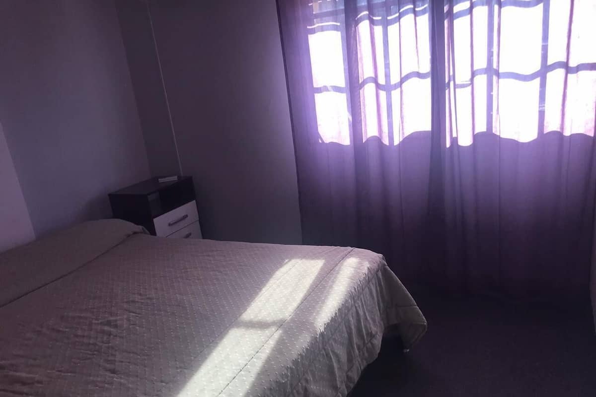 Une chambre à coucher avec un lit, une table de chevet et une fenêtre avec des rideaux.