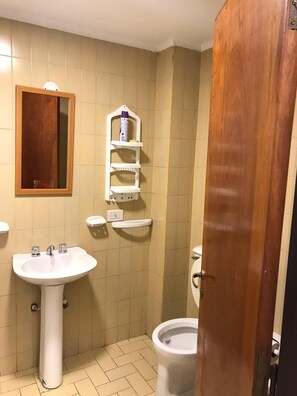 A bathroom with a pedestal sink, a toilet, and a wooden door. - Departamentos Belgrano (Salta)