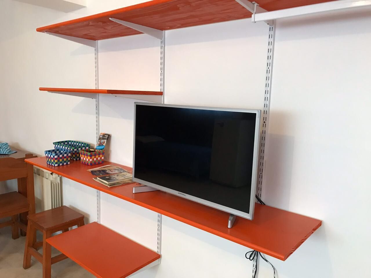 A room with a TV on a shelf, a desk with a chair, and storage boxes.