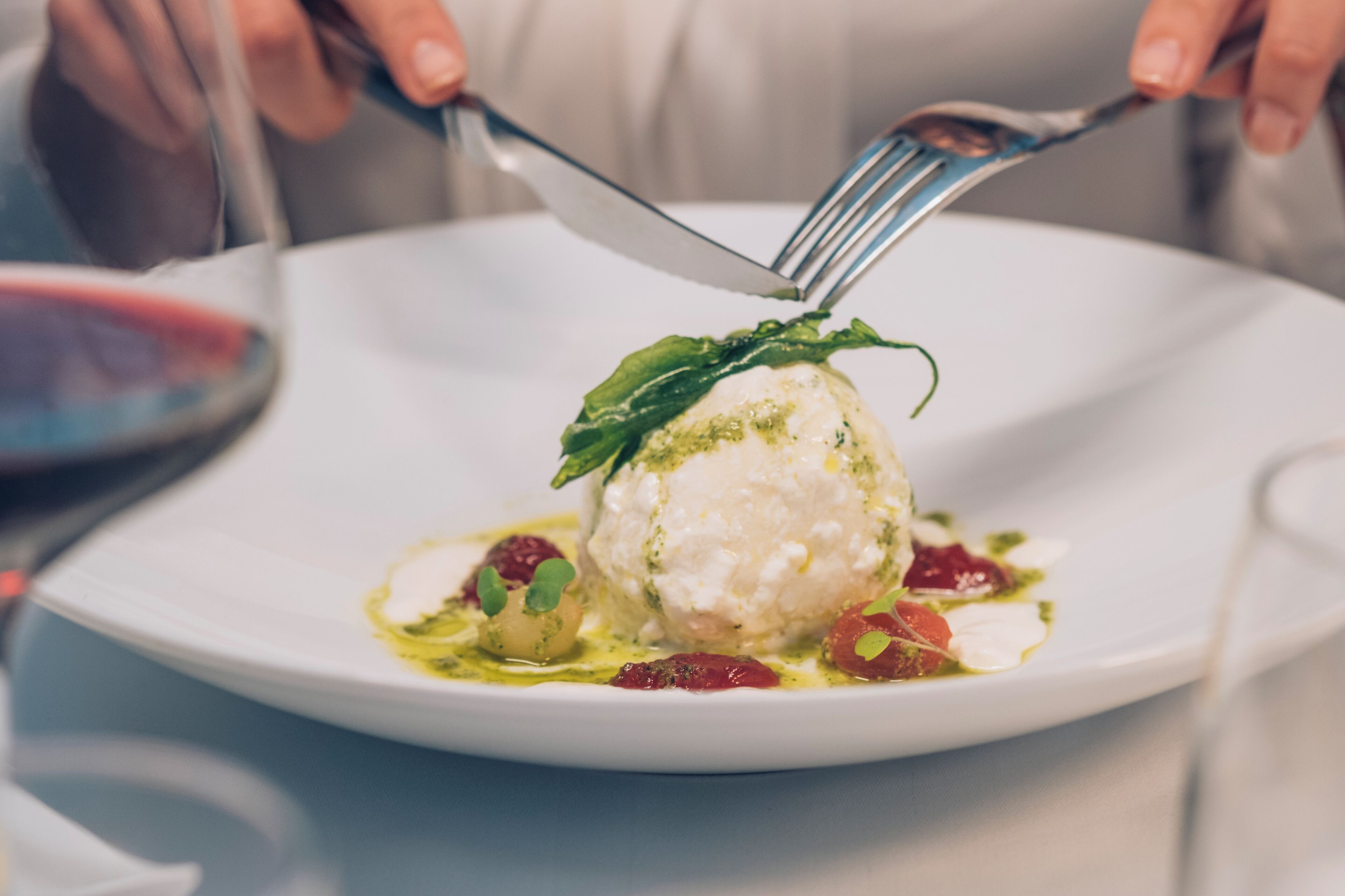Un plat blanc amb una culleradeta de gelat decorat amb una fulla i microverds, acompanyat d'una forquilla i un ganivet.