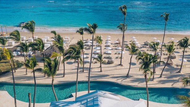 Un complexe hôtelier en bord de mer, doté d’une piscine, de palmiers et de chaises longues.