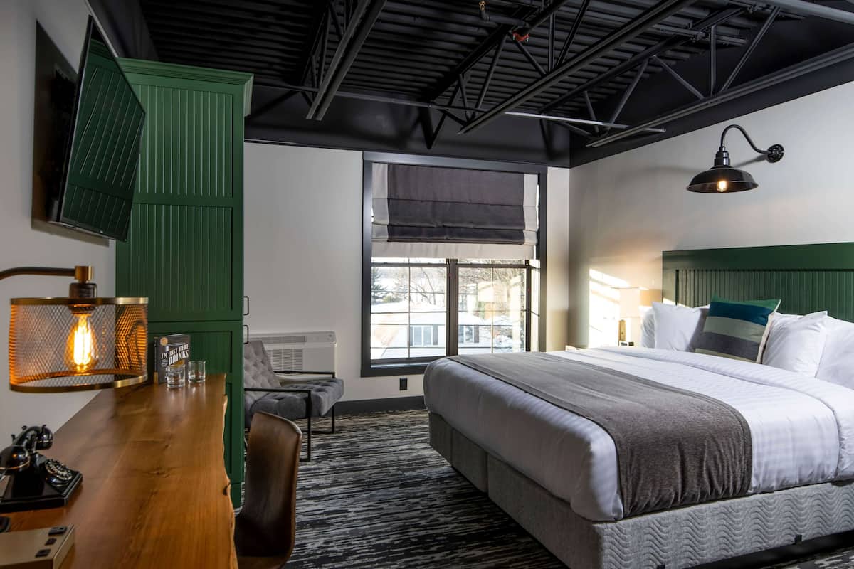 A hotel room with a large bed, a desk with a lamp, a chair, and a window with a view.