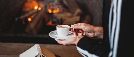 A person holding a cup of coffee near a fireplace with logs.
