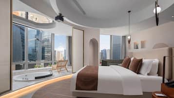 A modern hotel room with a large bed, a sitting area with a view of the cityscape, and a separate bathroom with a bathtub.