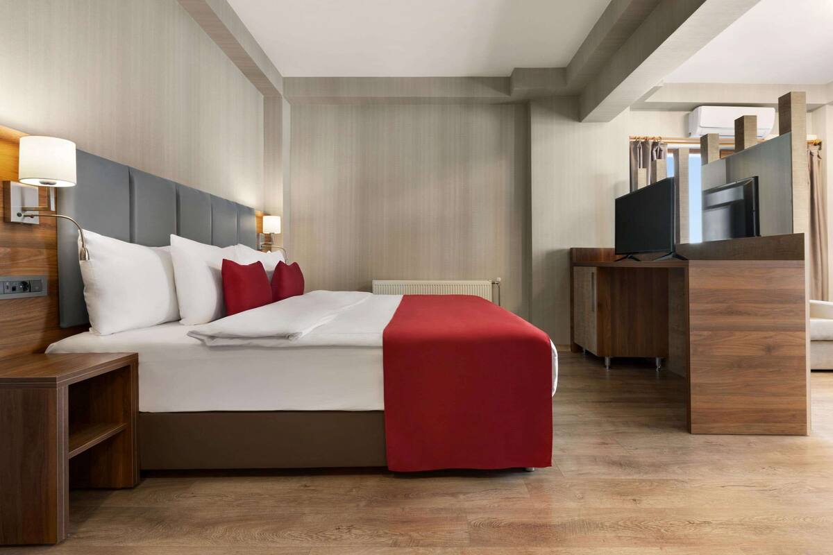 A modern hotel room with a large bed, a flat-screen TV, and a wooden desk.