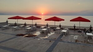 A terrace with tables and red umbrellas overlooking a sunset over the sea. - Ramada by Wyndham Van (Edremit)