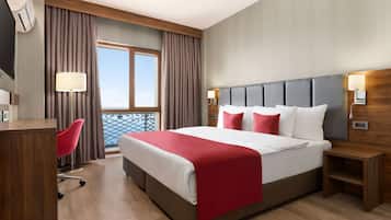 Habitación de hotel con una cama grande, un escritorio, una silla, una ventana con cortinas y vistas al balcón.
