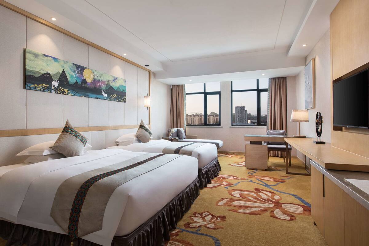 Une chambre d’hôtel avec deux lits, un bureau, une télévision et une grande fenêtre donnant sur la ville.