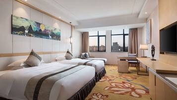 A hotel room with two beds, a desk, a TV, and a large window with a city view.