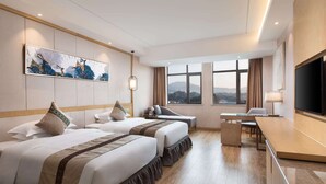 Hotelkamer met twee bedden, een bureau, een televisie en een groot raam met uitzicht op de bergen.