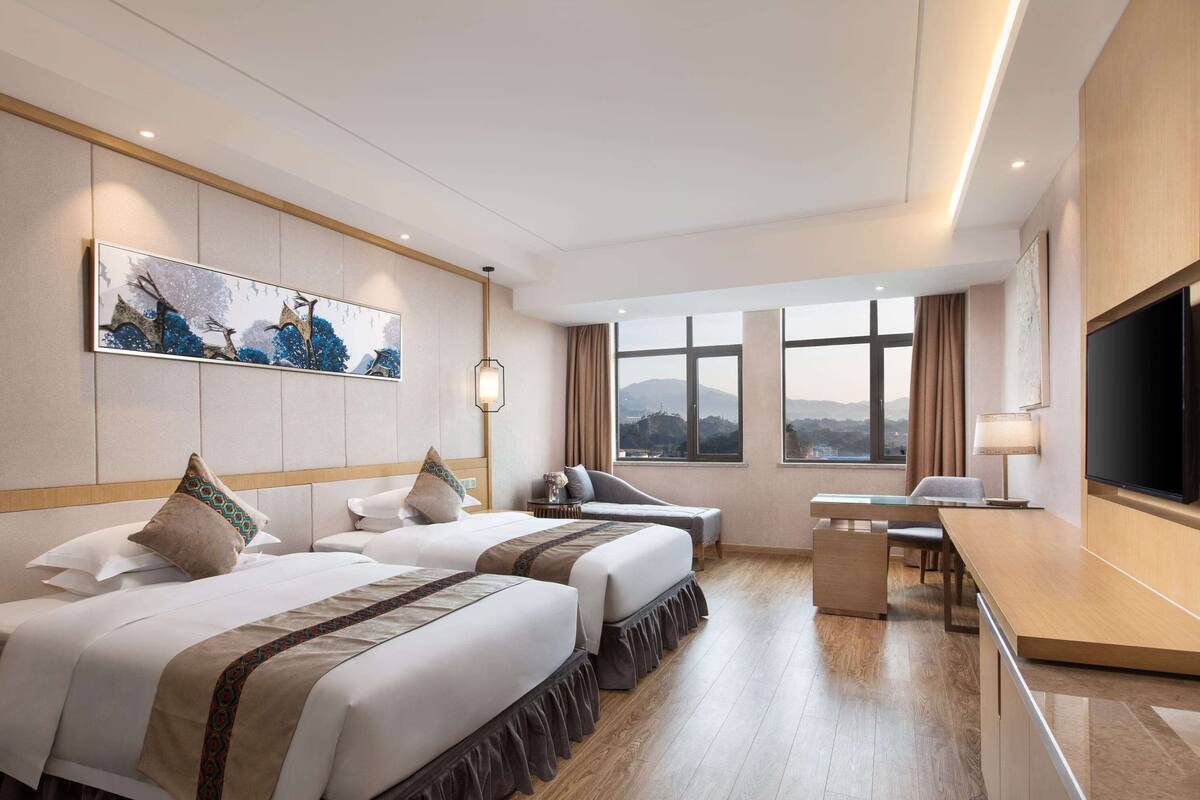 Une chambre d’hôtel avec deux lits, un bureau, une télévision et une grande fenêtre donnant sur les montagnes.