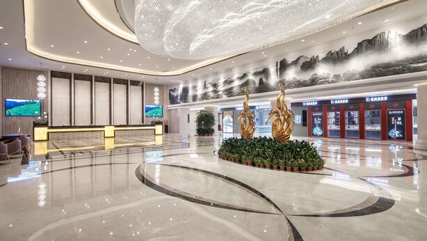 Een ruime lobby met een modern design, met een groot digitaal scherm, een receptiebalie en een decoratieve plantenstelling.