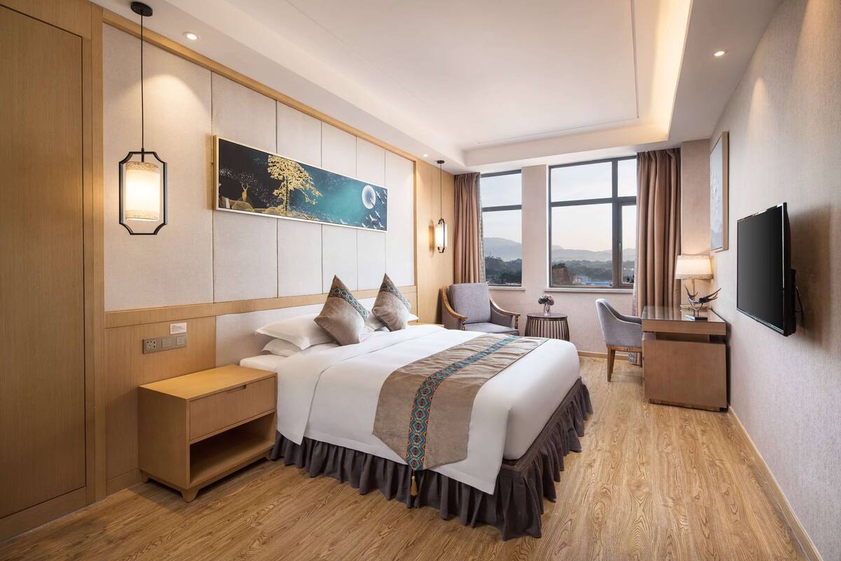 Une chambre d’hôtel avec un grand lit, des tables de chevet, un bureau, une chaise, une télévision et une fenêtre donnant sur un beau paysage.