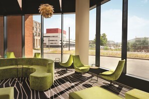A modern interior with a green sofa set, a patterned floor, and large windows offering a view of the street. - Super 8 by Wyndham Mainz Zollhafen (Mainz)
