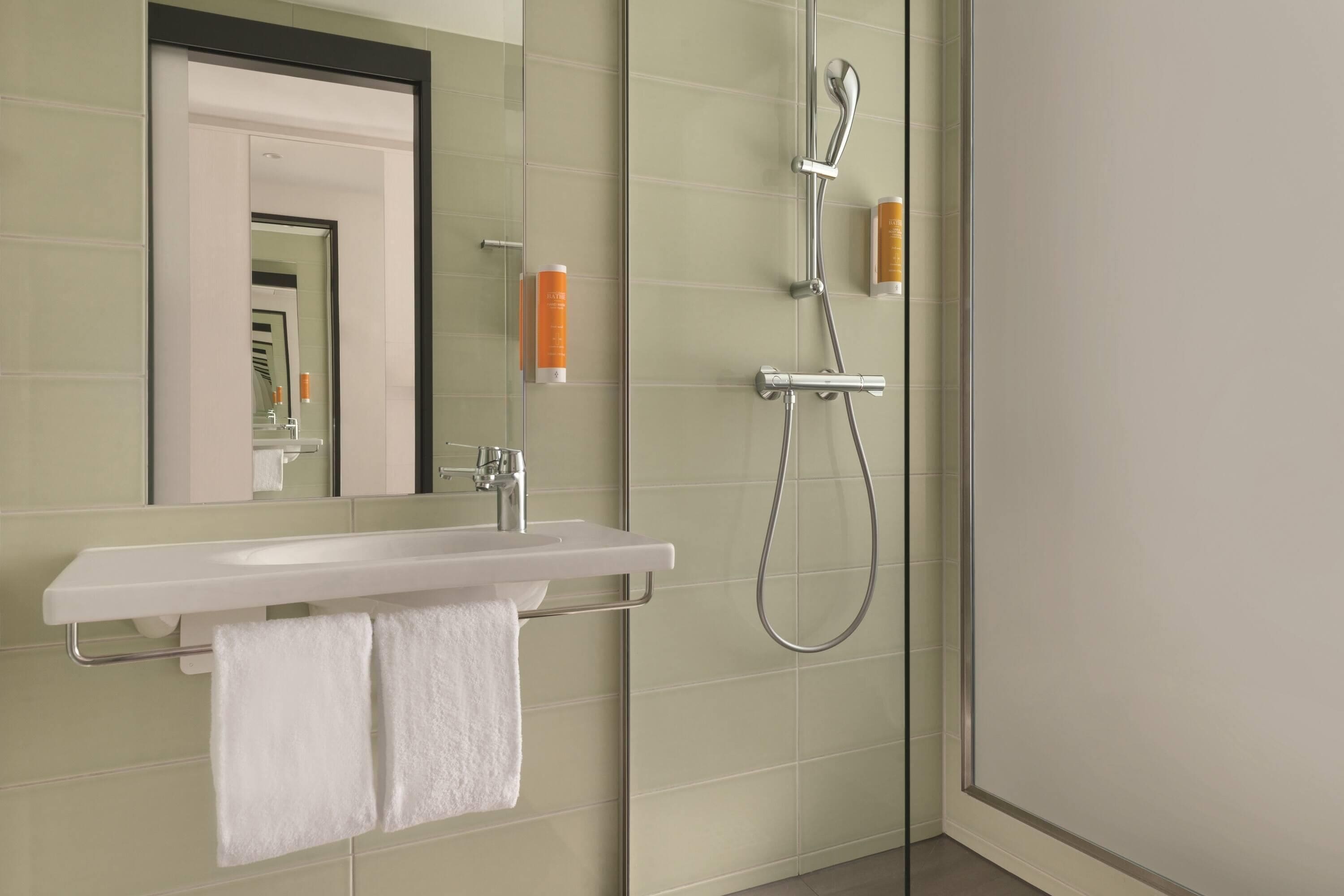 Ein modernes Badezimmer mit Duschkabine aus Glas, einem weißen Waschbecken und einem Spiegel darüber.