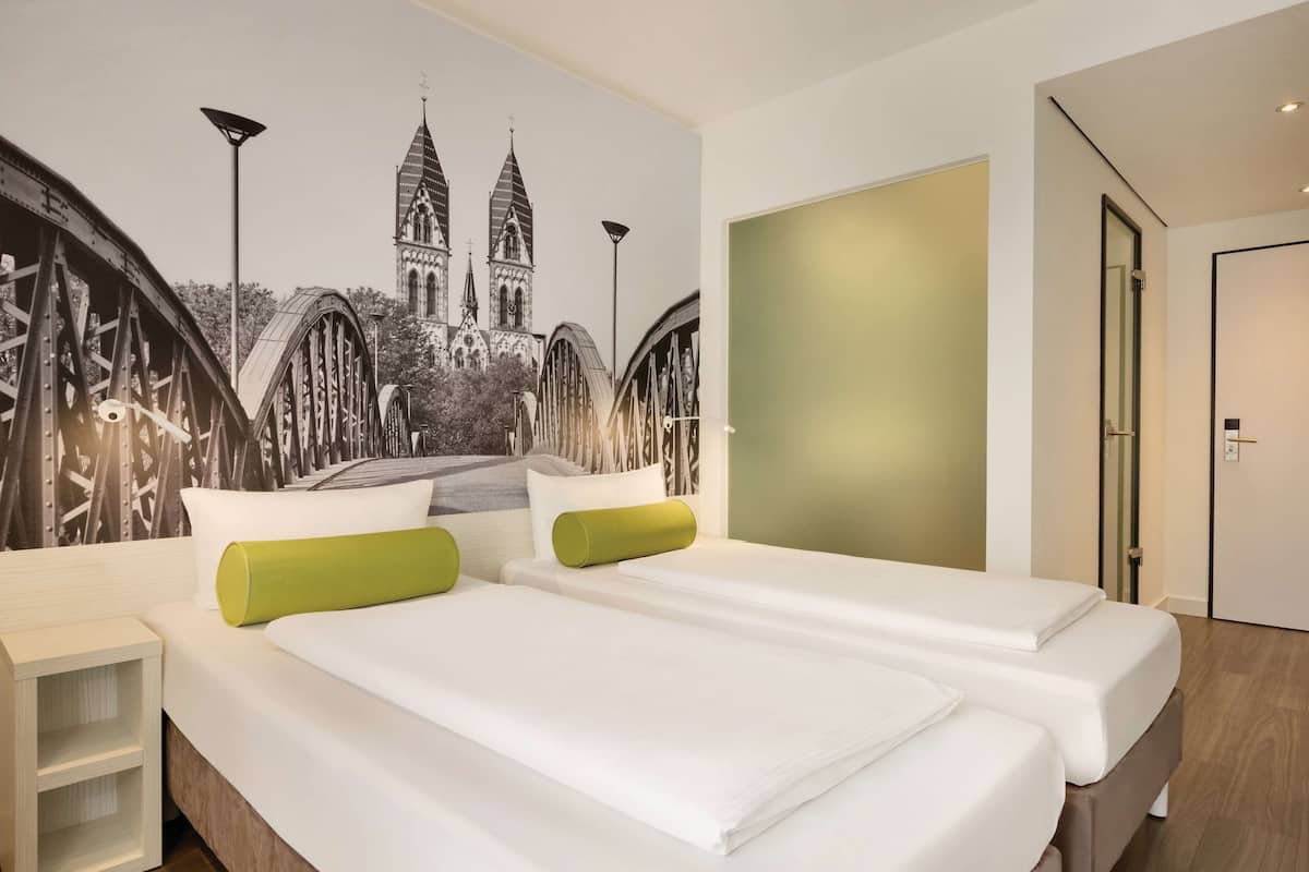 Une chambre d’hôtel avec deux lits, une fresque représentant une cathédrale, un mur végétal et une porte.