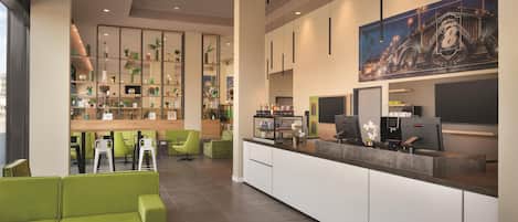 A modern hotel lobby with green seating, a reception desk, and a large cityscape painting.