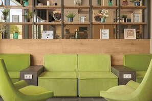 A reception area with a green sofa, a wooden reception desk, and a shelf with various decorative items and signs. - Super 8 by Wyndham Mainz Zollhafen (Mainz)