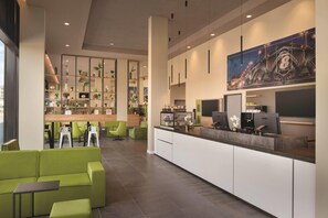 Een moderne hotelentree met groene zitplaatsen, een receptiebalie en een koffiebar.