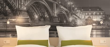 A hotel room with a bed, two pillows, and a wall mural of a bridge.