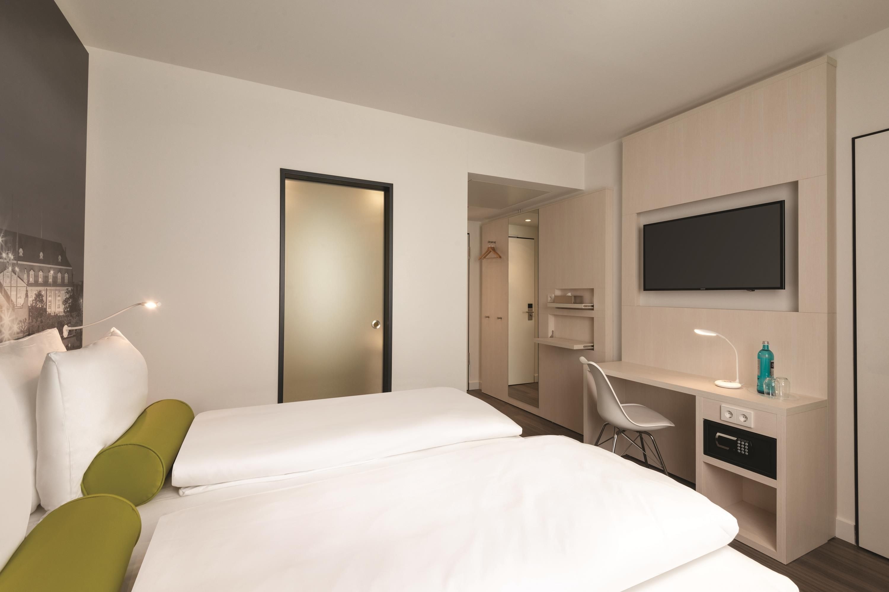 Ein Hotelzimmer mit Bett, Schreibtisch, Stuhl, Fernseher und Minibar.
