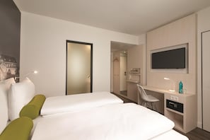 A hotel room with a bed, a desk, a chair, a TV, and a minibar.