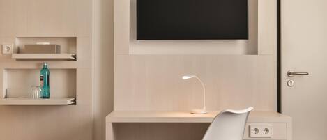 Una habitación de hotel con una cama, un escritorio con televisor, una silla, una lámpara y un panel de control.