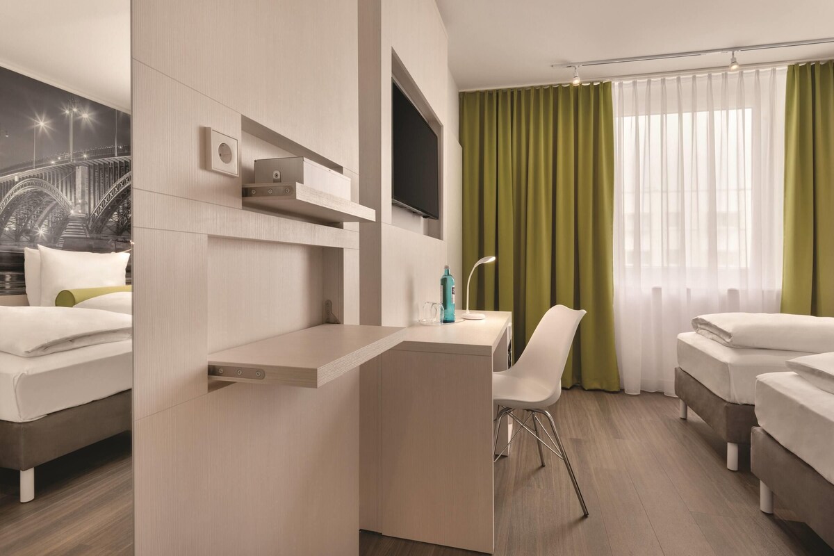 Een hotelkamer met een bed, een bureau, een stoel, een televisie en een raam met gordijnen.