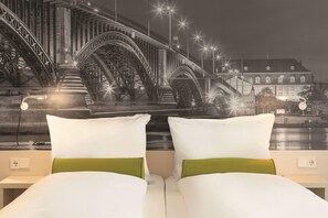 Een slaapkamer met twee bedden, elk met witte lakens en een groen kussen.