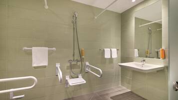 Ein modernes Badezimmer mit grünen Fliesen, einem weißen Waschbecken, einem Spiegel und einer Dusche mit Duschbrause.