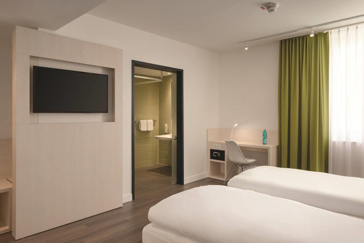 Een hotelkamer met een bed, een bureau, een stoel, een televisietoestel en een badkamer die door een open deur zichtbaar is.