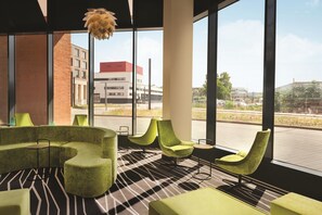 Een modern interieur met een groene zithoek, een vloer met patroon en grote ramen met uitzicht op gebouwen en een straat.