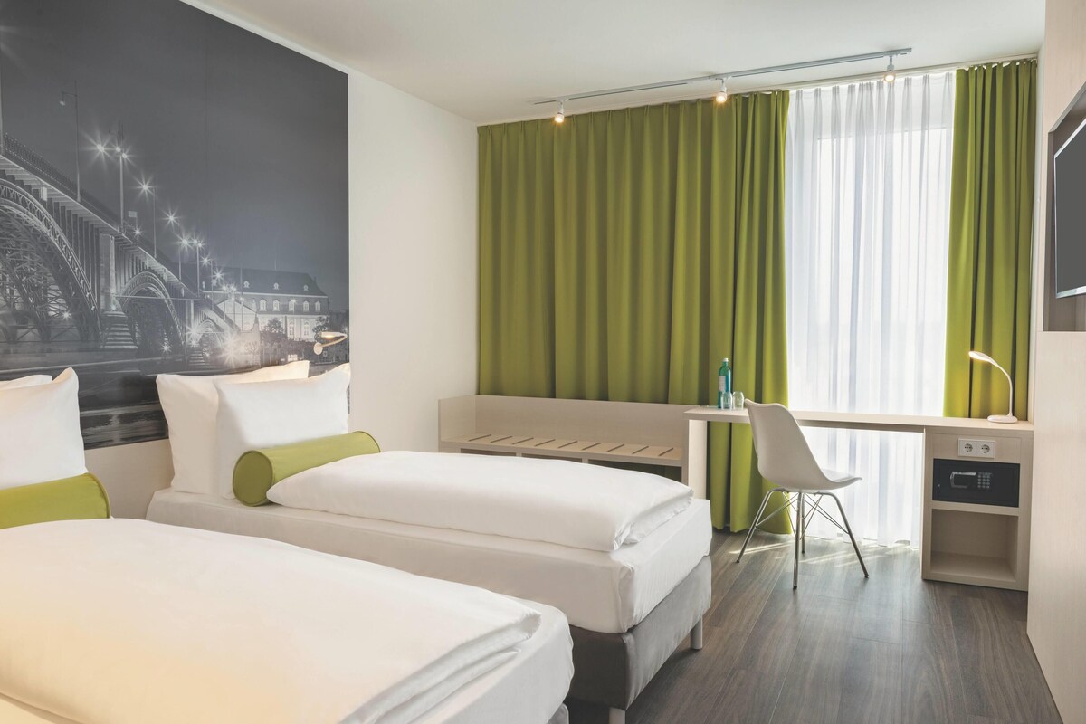 Een hotelkamer met twee bedden, een bureau, een stoel en een groot raam met gordijnen.