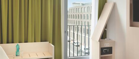 Habitación de hotel con cama, escritorio, silla, ventana y vista a edificios, además de un mini bar.