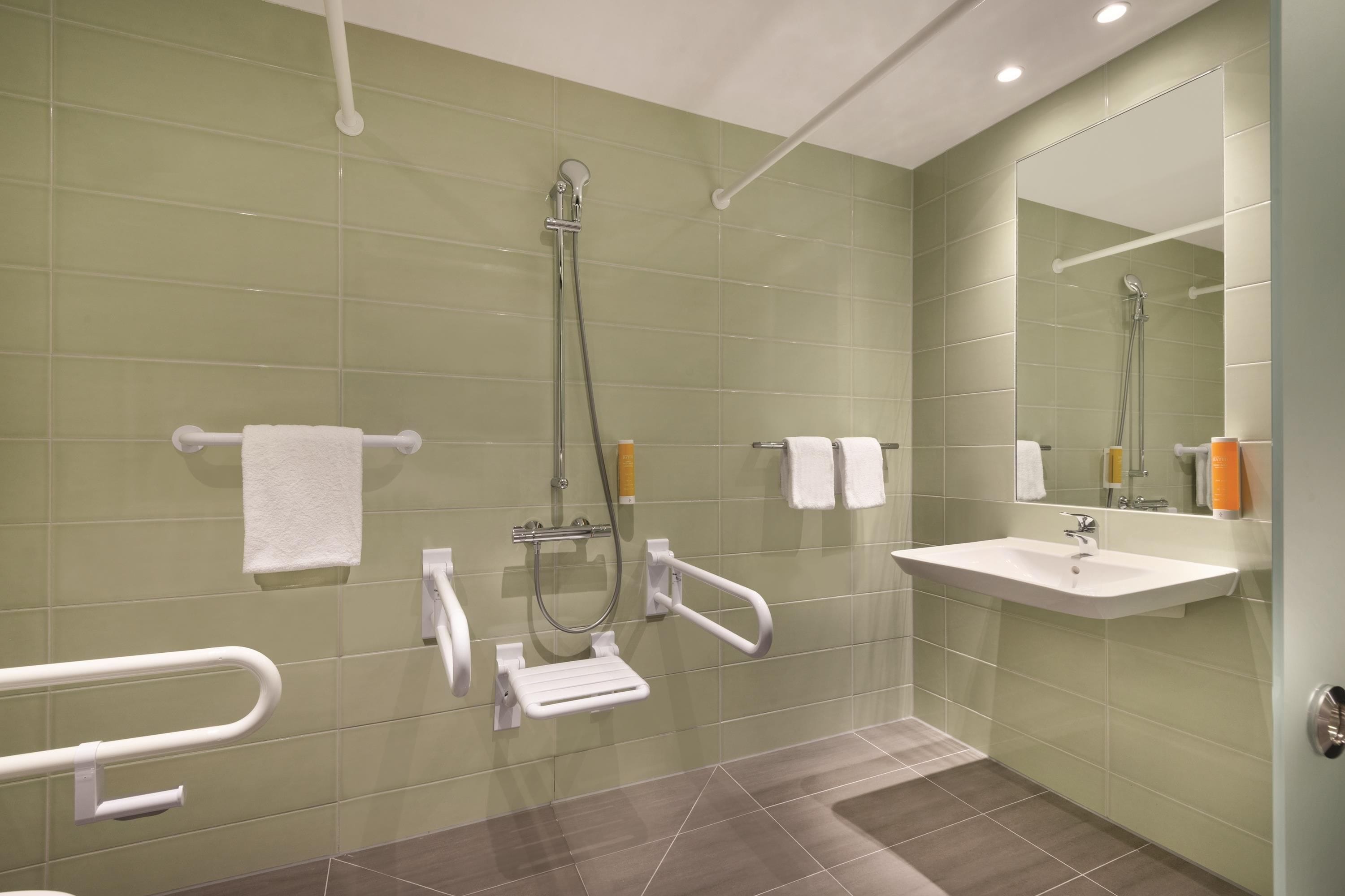 Ein modernes Badezimmer mit grünen Fliesen, einem weißen Waschbecken, einem Spiegel und einer Dusche mit Duschbrause.