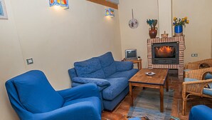 Ett vardagsrum med en blå soffa, ett träbord, en tv och en öppen spis.