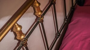 En närbild på en sängram i metall med utsmyckade detaljer i guld och ett rosa sängöverkast.