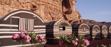 A row of striped, arched structures with a rocky cliff in the background.