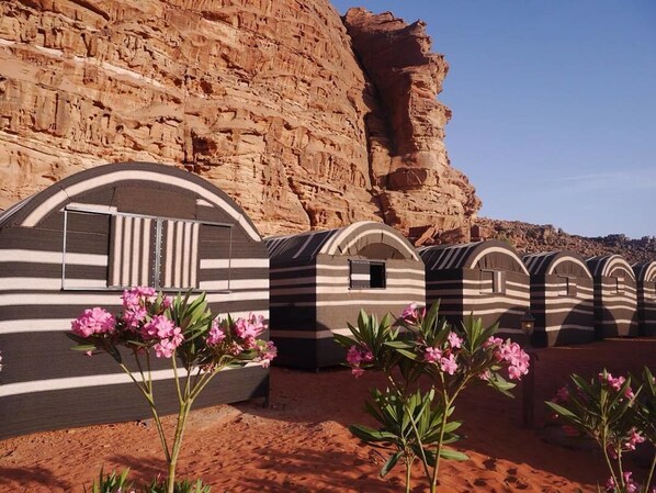 A row of striped, arched structures with a rocky cliff in the background.