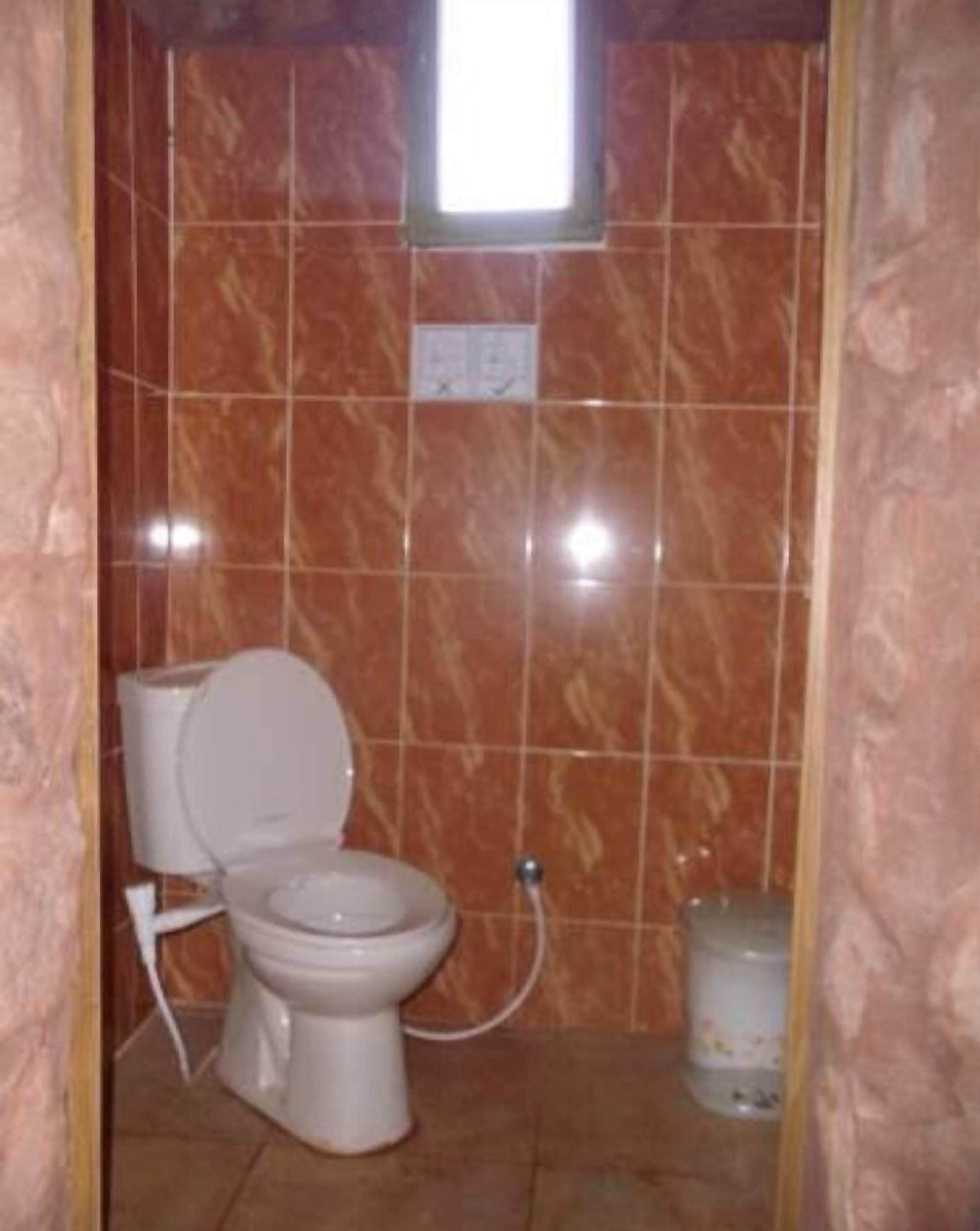A small bathroom with a toilet, a wall-mounted sink, and a trash can.