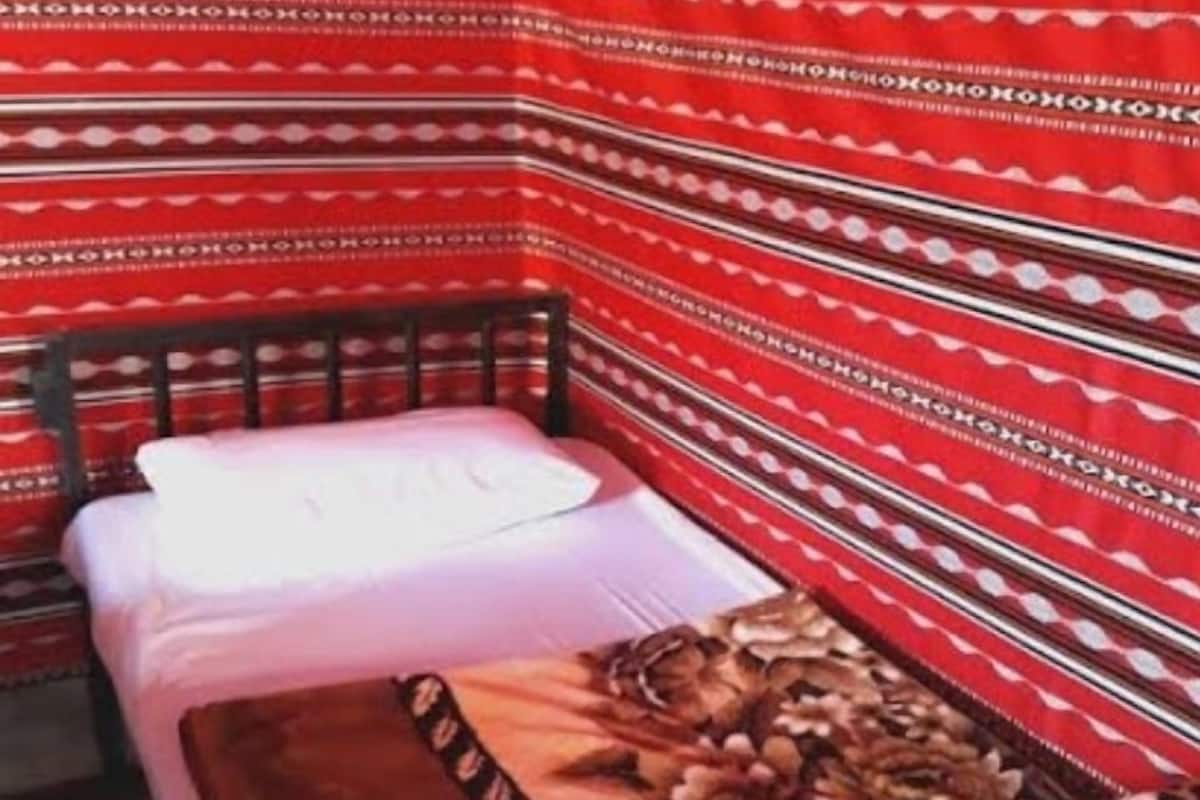 A small, cozy room with a single bed, a wooden headboard, and a patterned red and white wall.
