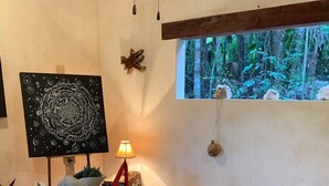 A dining area with a long wooden table, chairs, a decorative rug, and a view of greenery through a window. - Hotel Buenavista Bacalar Jungle Experience (Bacalar)