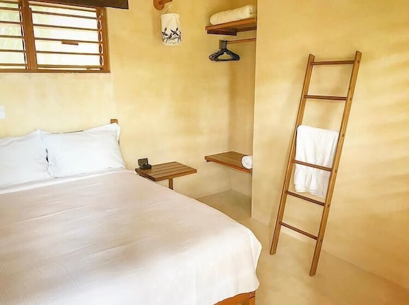 A bedroom with a bed, a nightstand, a wooden ladder, a hanging light fixture, and a window with blinds.
