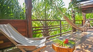 A wooden deck with a hammock, a wooden chair, and a small table with a plant. - Hotel Buenavista Bacalar Jungle Experience (Bacalar)