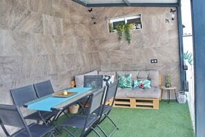 A patio area with a table and chairs, a cushioned seating area, and a small window with plants.