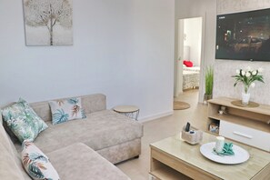 A modern living room with a beige sectional sofa, a small round table, a flat-screen TV, and a decorative plant.