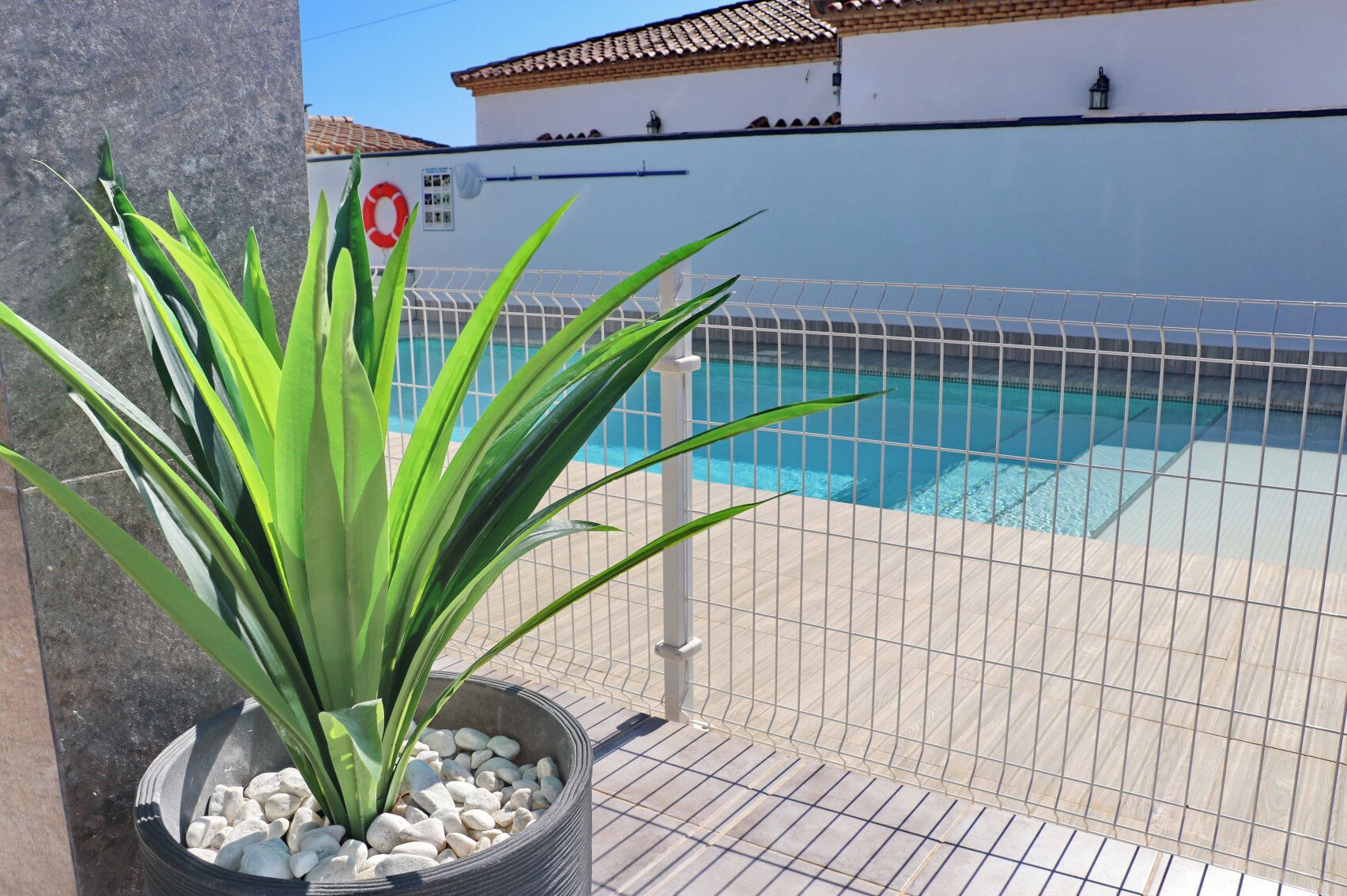 Un espace piscine doté d’une terrasse carrelée, d’une clôture en métal et d’une plante en pot aux feuilles vertes.